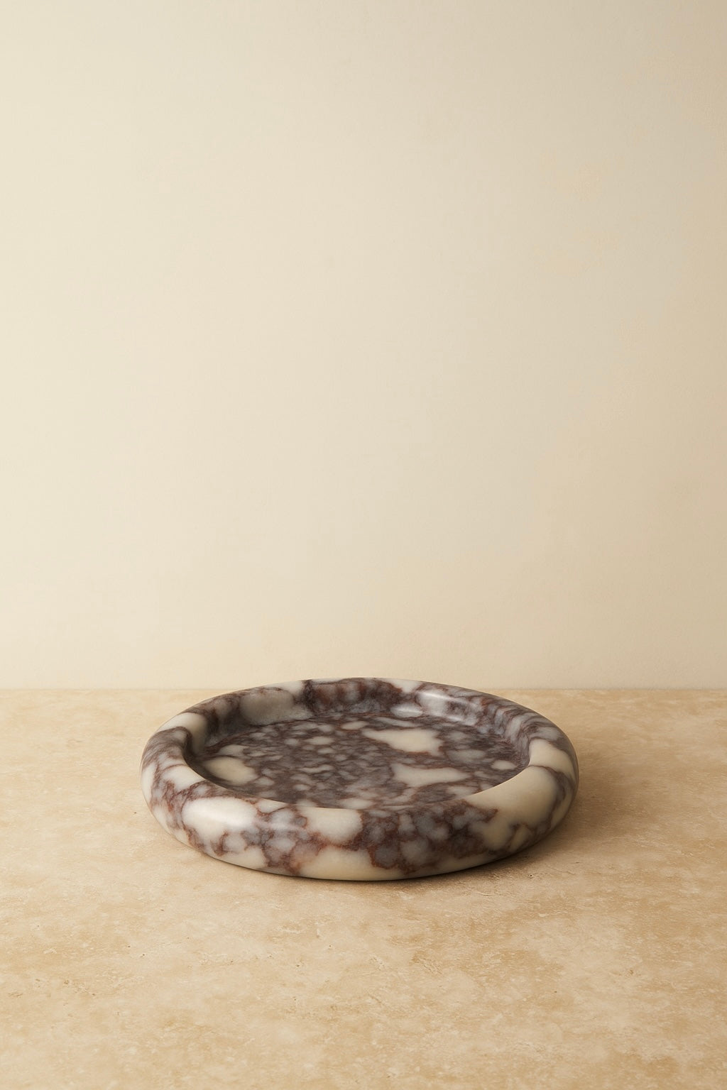 Round Calcutta marble-patterned trinket dish on a beige surface with a beige background