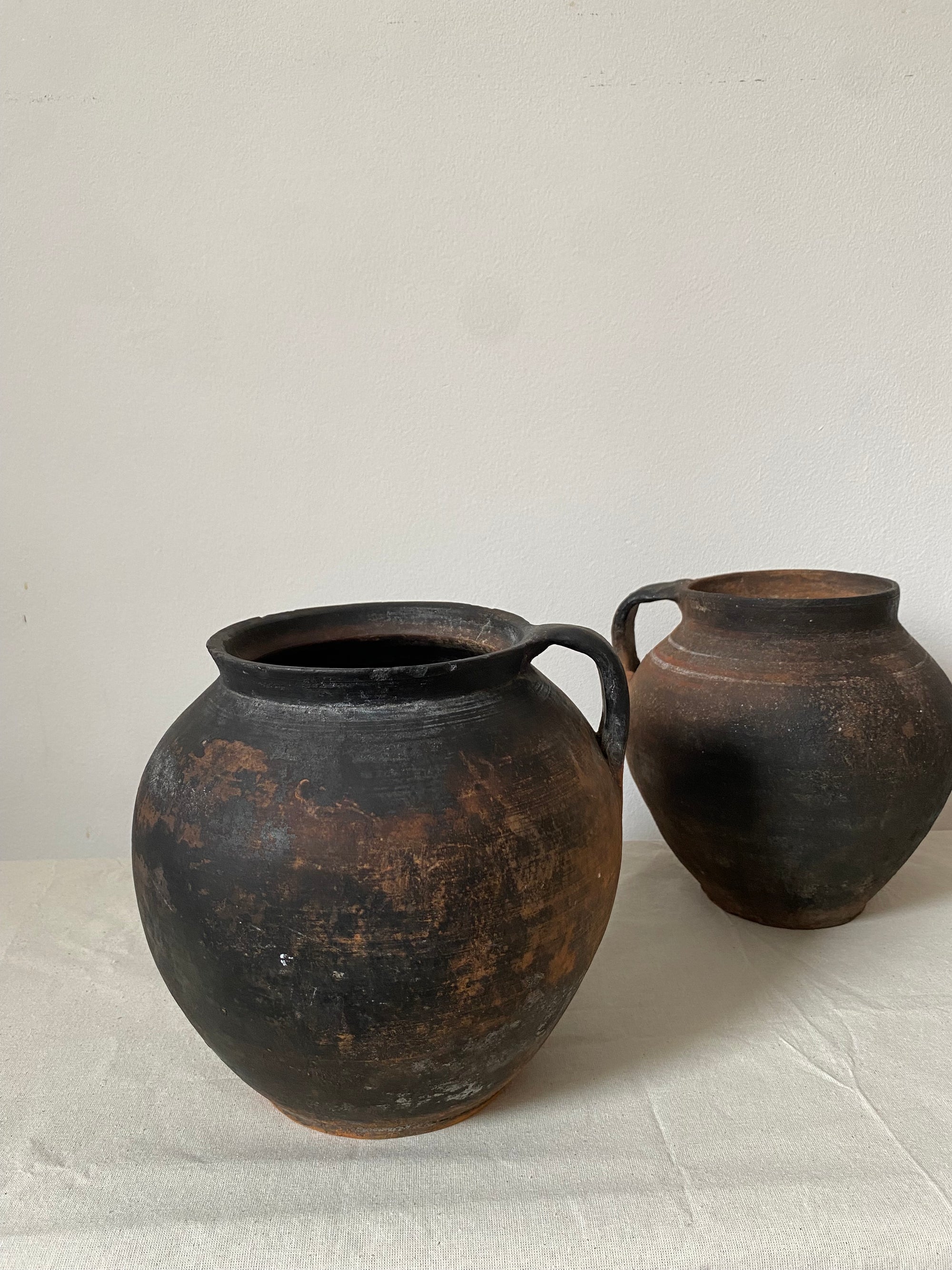 Two rustic antique clay pots on a textured white surface