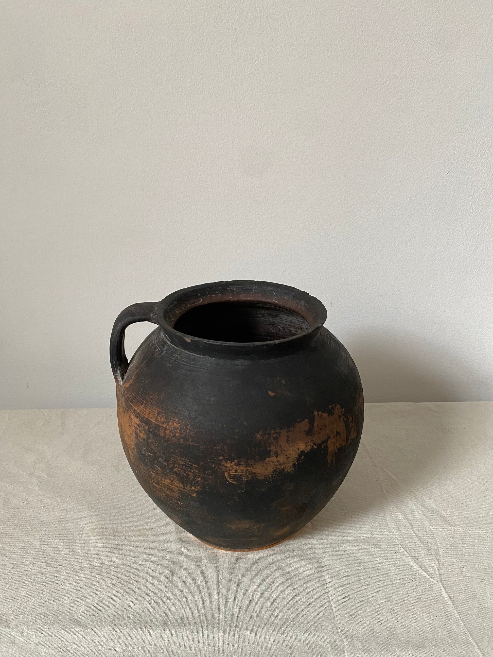 Black terracotta pot with a textured surface on a light gray background.
