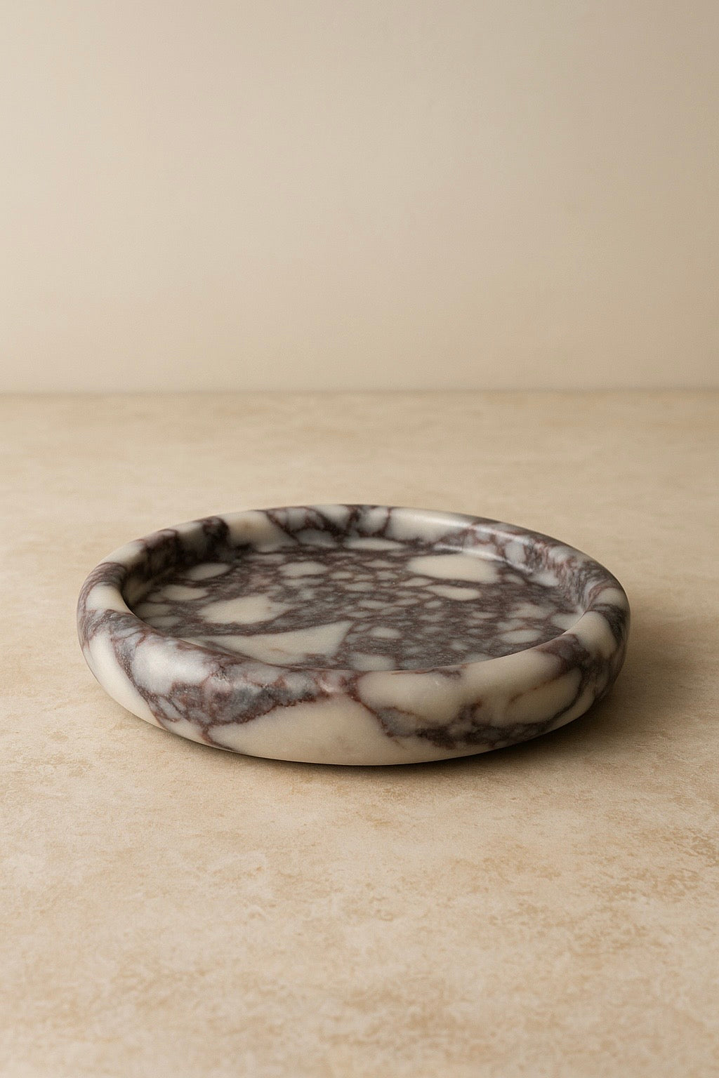 Round Calcutta marble-patterned ceramic dish on a beige surface with a neutral background