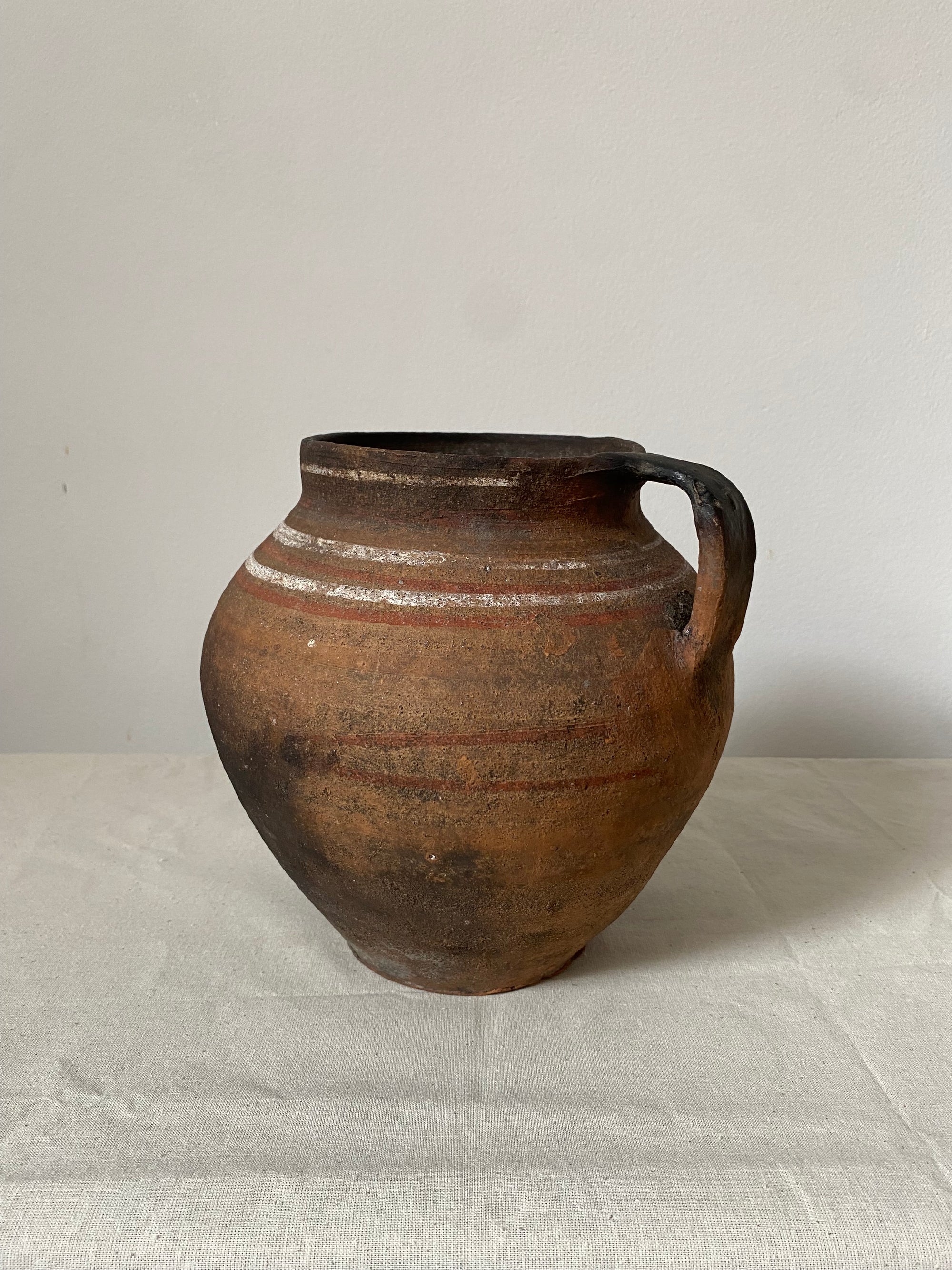 Brown ceramic vase with a handle on a light gray background