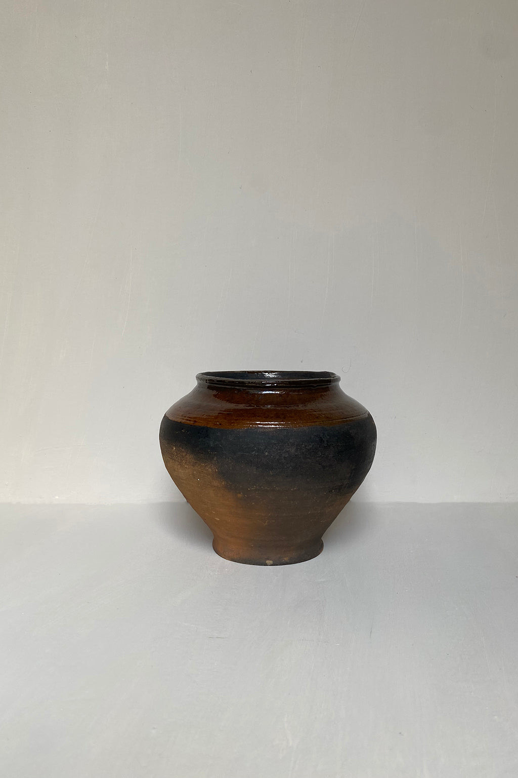 An antique hand-thrown small clay pot with a rich terracotta base, featuring subtle age-related textural changes and a rustic appearance.