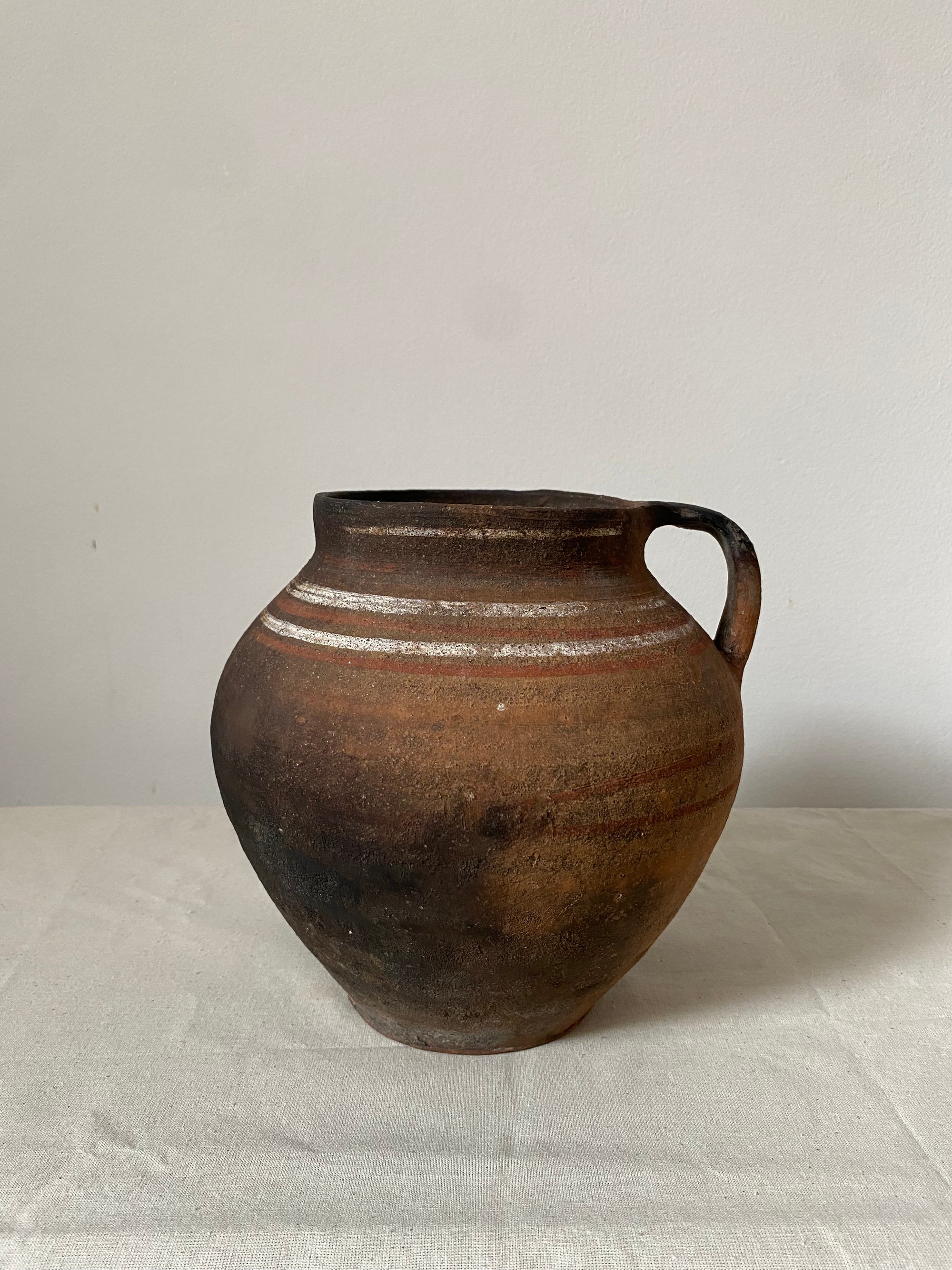 Brown earthenware vase with a handle on a light gray background