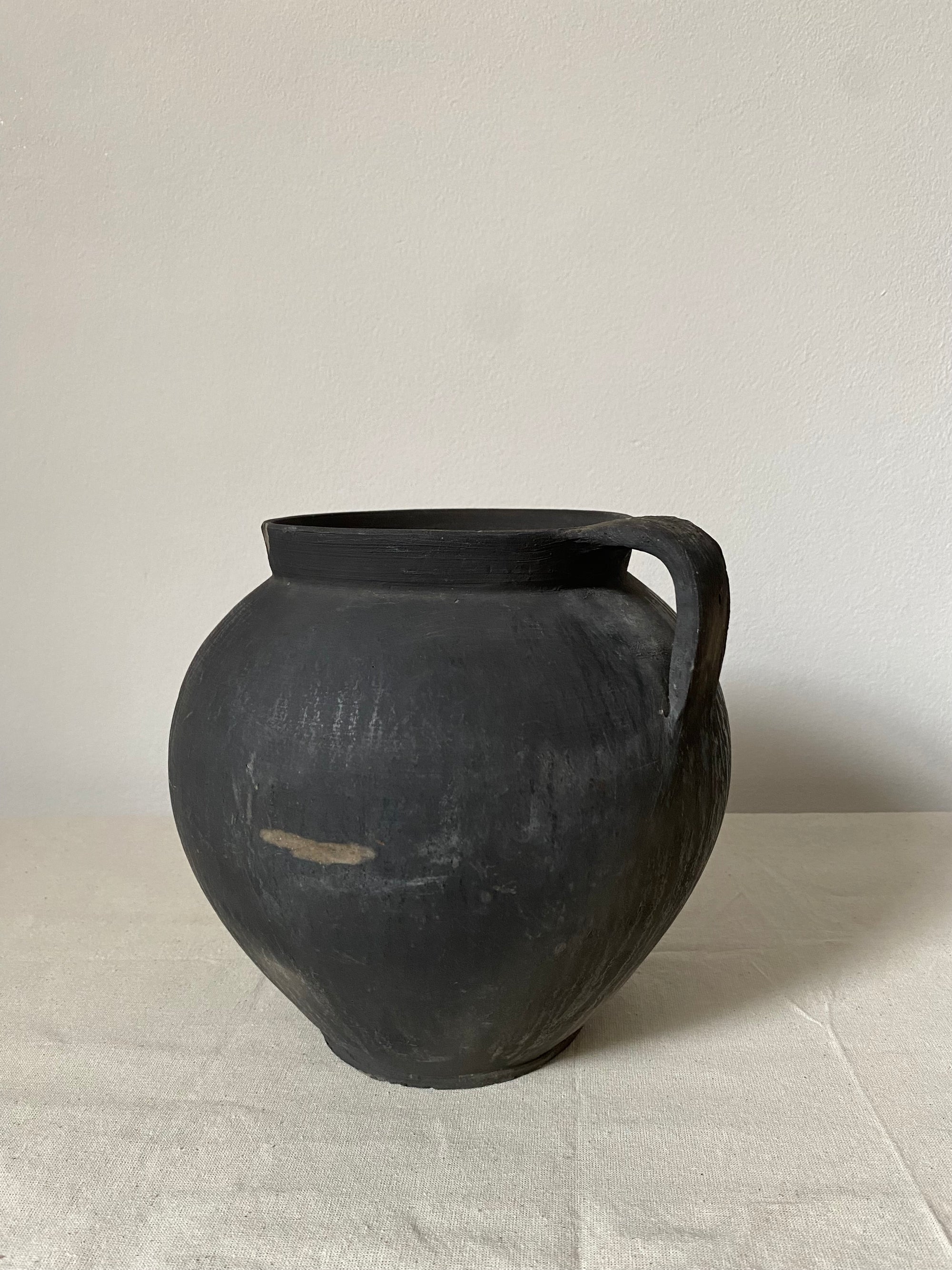 Black antique clay pot with a handle on a light grey background