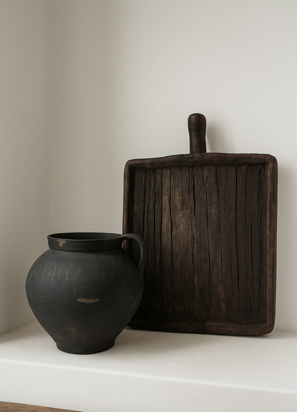 Black vase and wooden cutting board on a white surface with a neutral background