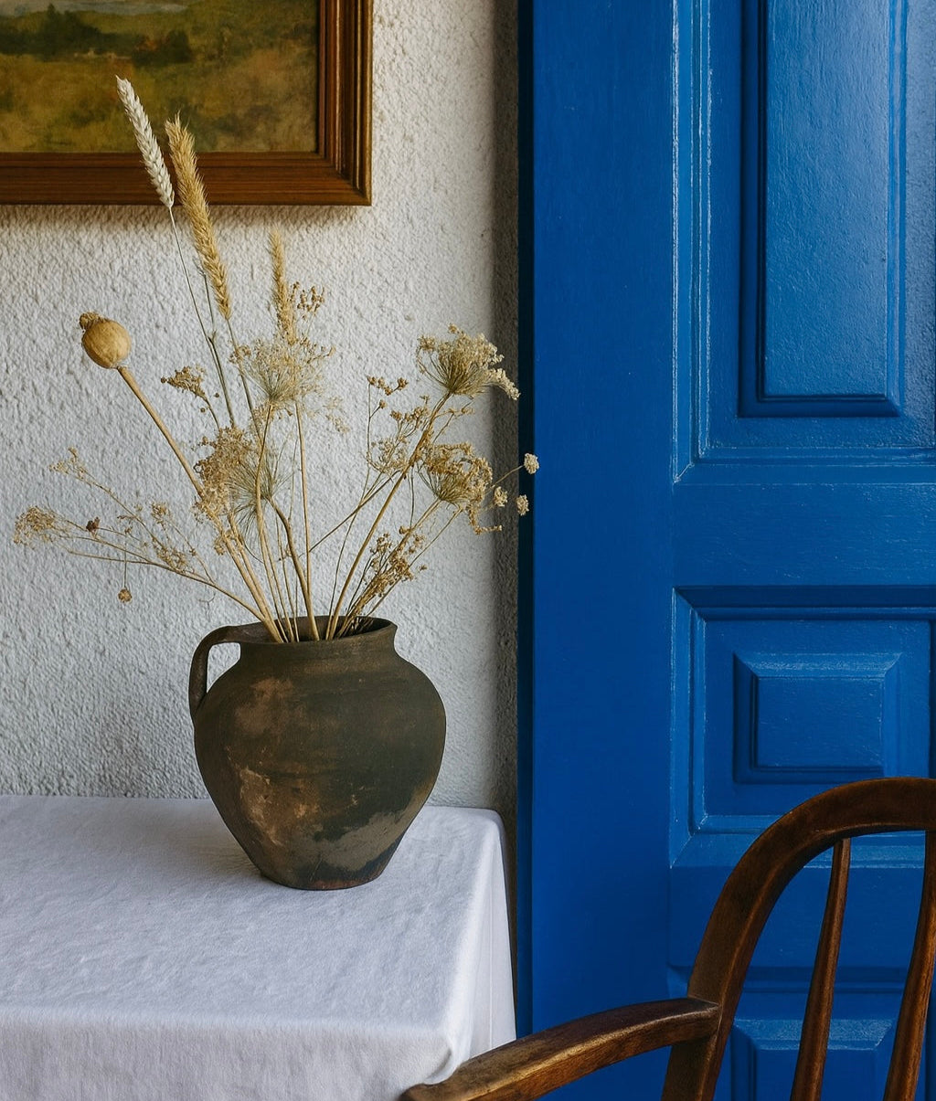 Antique Terracotta Clay Pot with dried flowers on a table next to a blue door