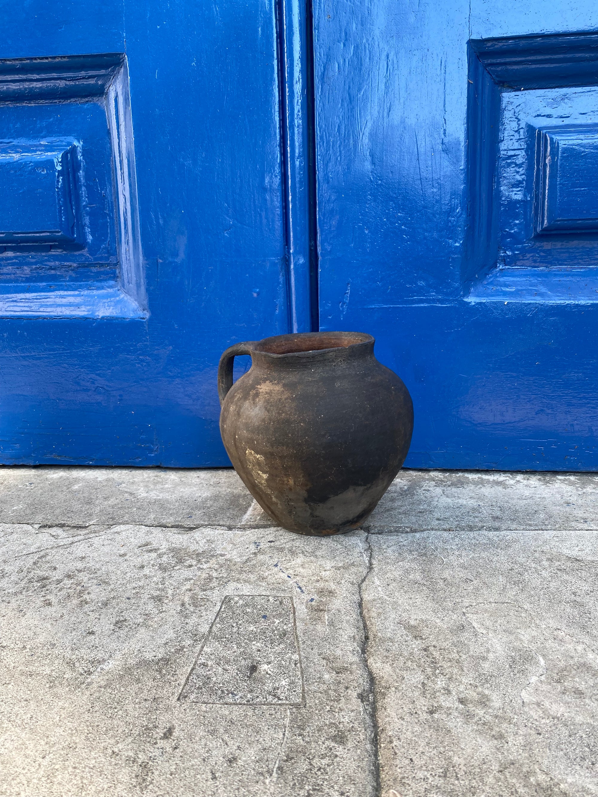 Black Antique Terracotta Clay Pot on a stone surface in front of a blue door